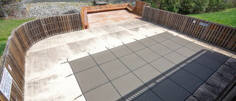A covered patio area with a concrete floor, wooden deck, and a metal fence.