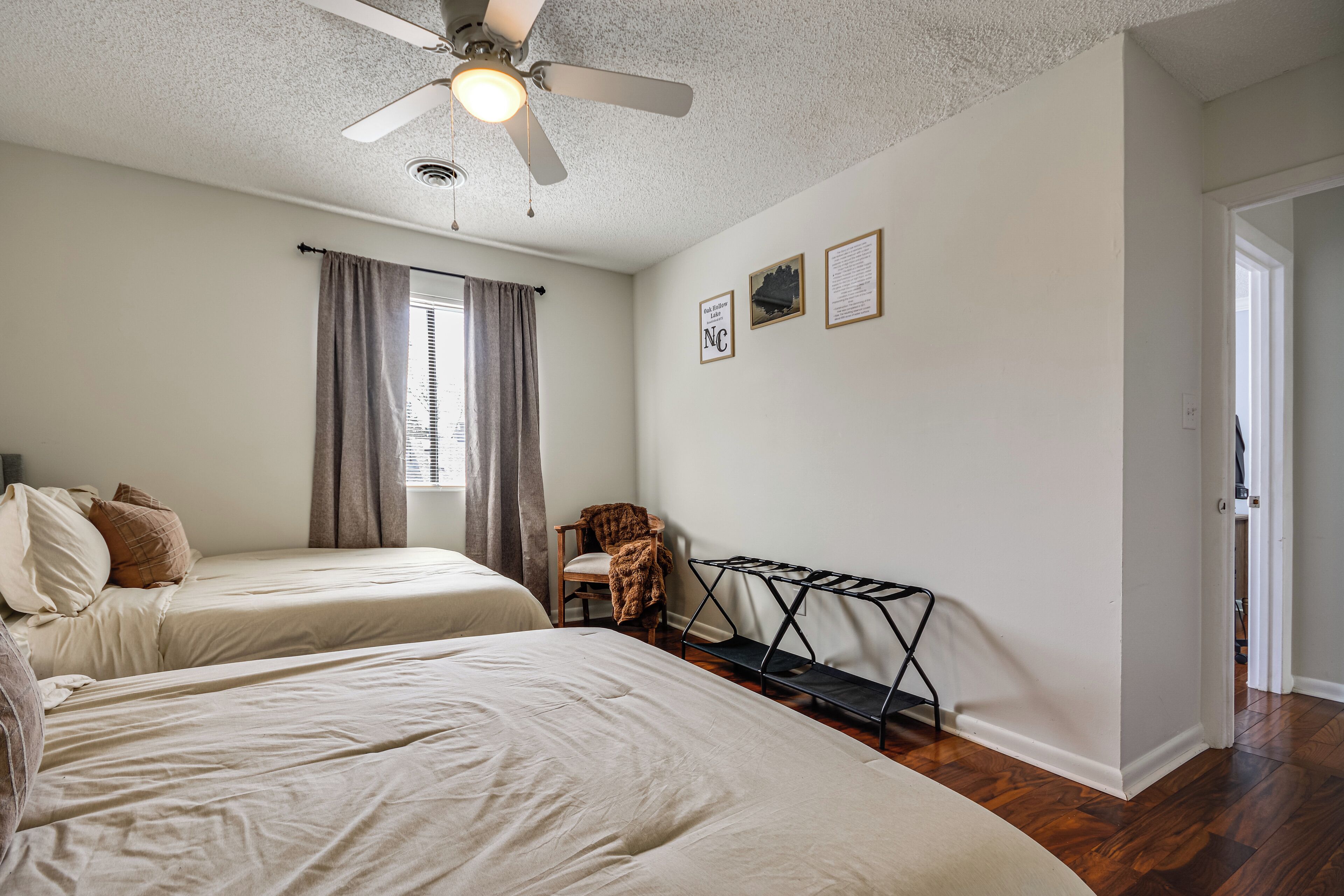 A bedroom with two beds, a ceiling fan, a window with curtains, a chair, and a wall-mounted rack.