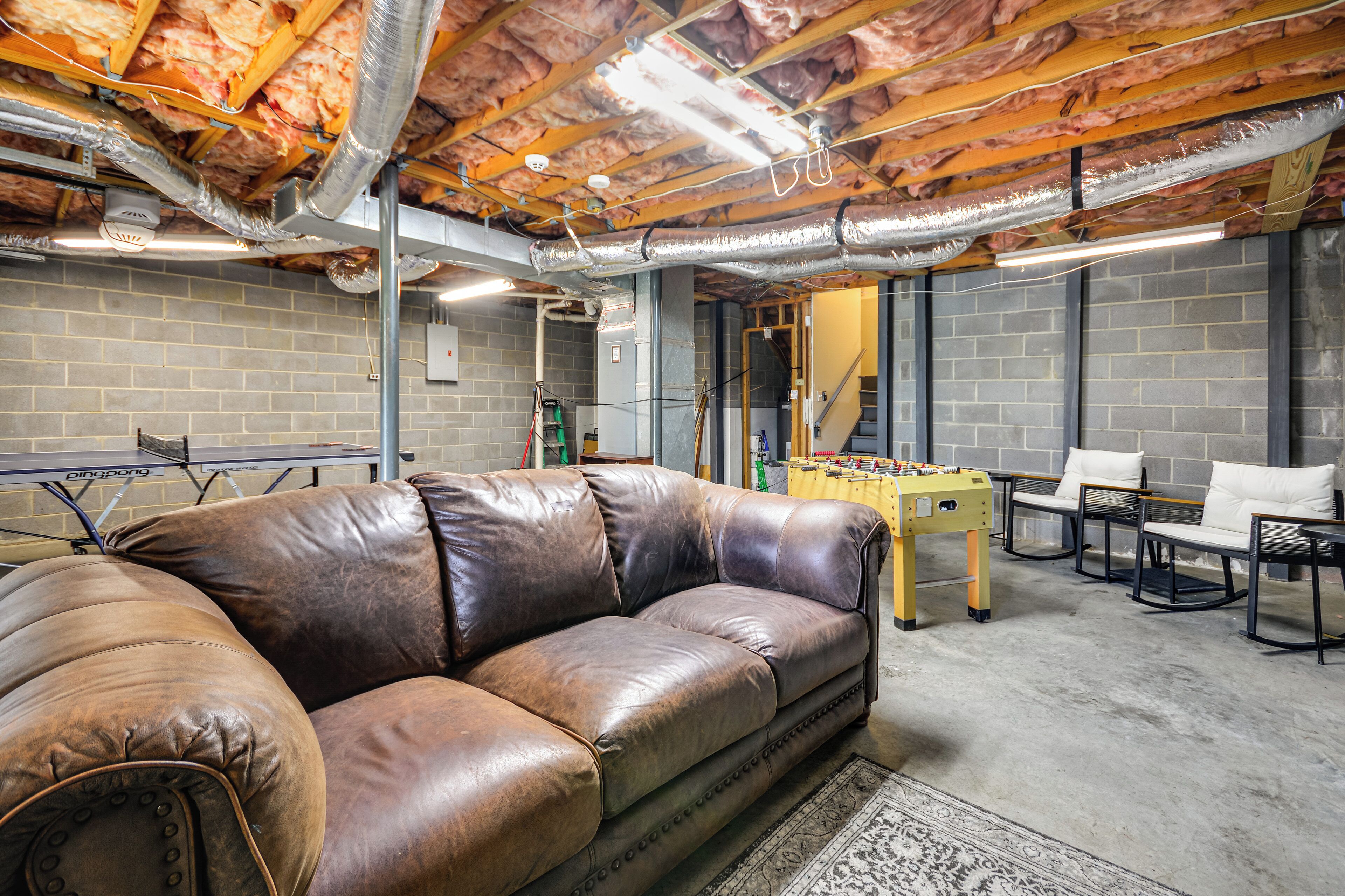 A room with a leather couch, a foosball table, and a brick wall.