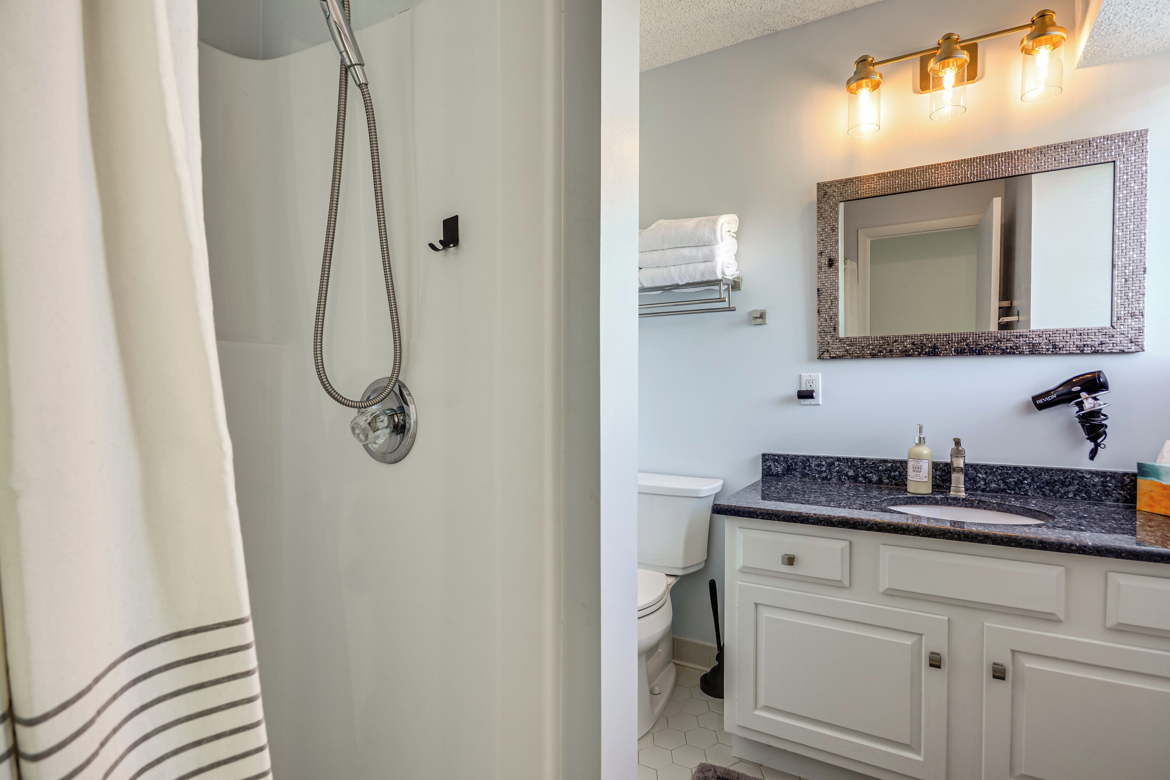 Ein Badezimmer mit Dusche, Toilette, Waschtisch, Spiegel und Handtuchhalter.