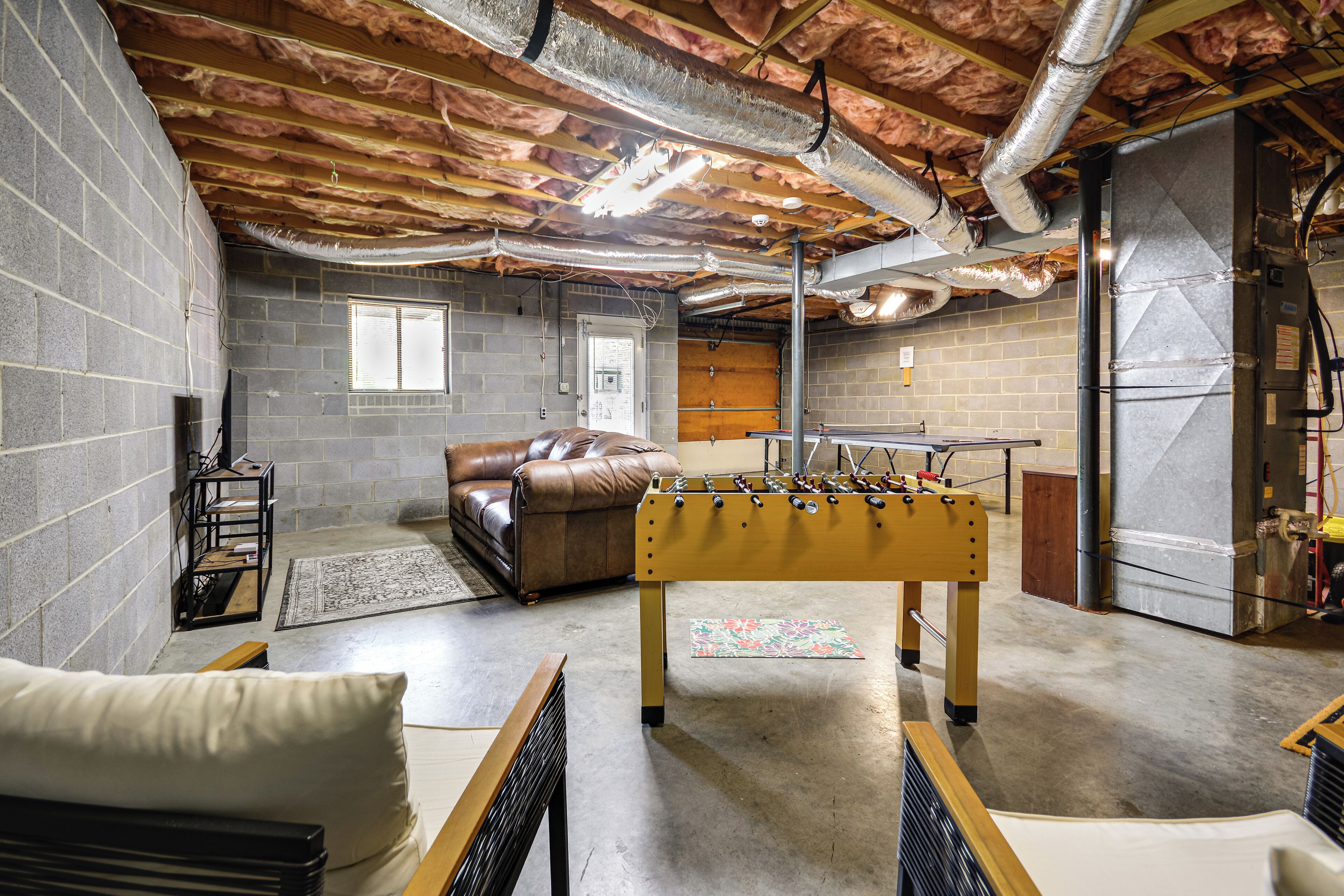 A basement with exposed brick walls, a foosball table, a leather couch, and a window.