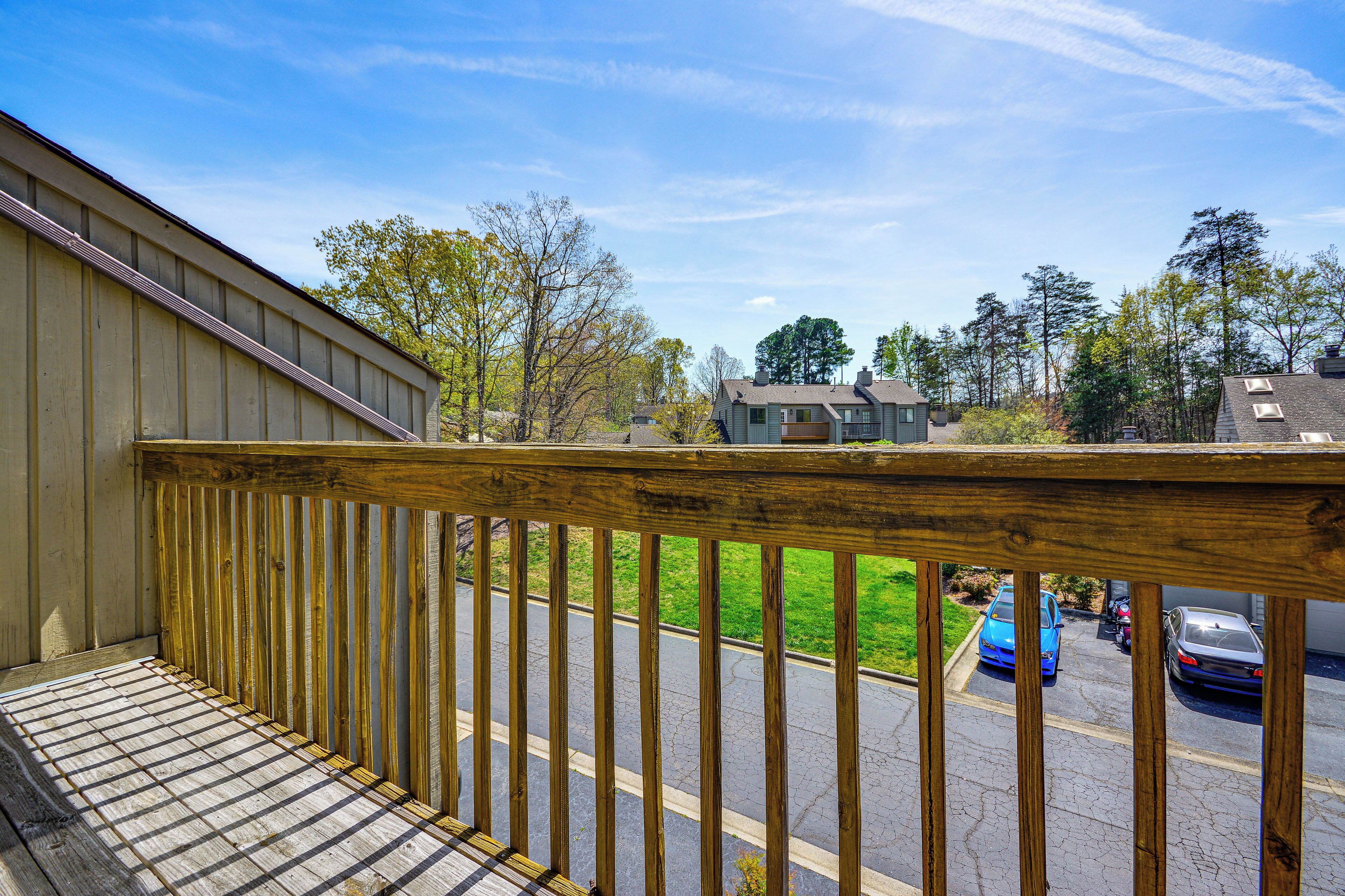 A wooden balcony with a view of a parking lot and houses.
