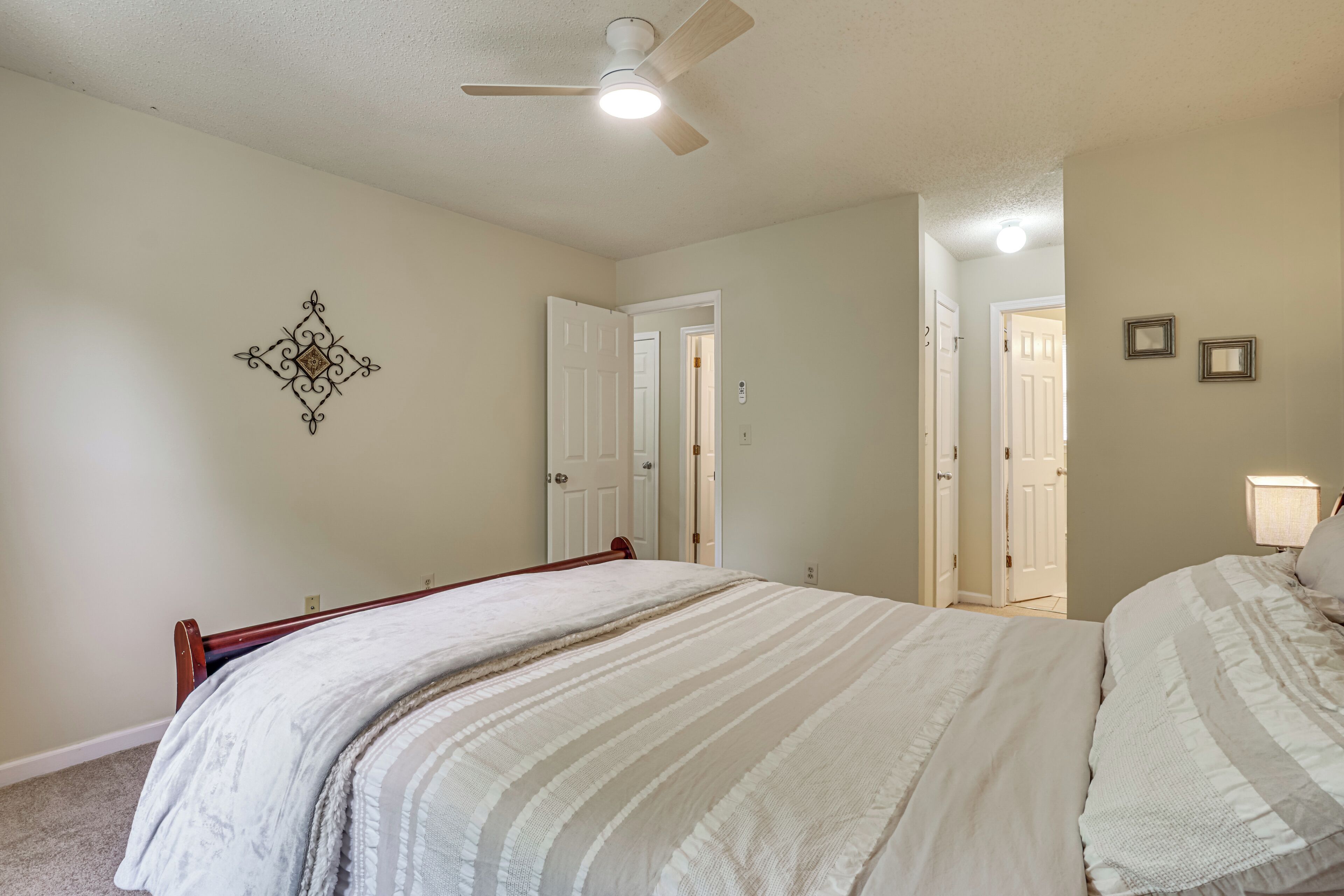 A bedroom with a bed, a ceiling fan, a wall-mounted decorative piece, and a door leading to another room.
