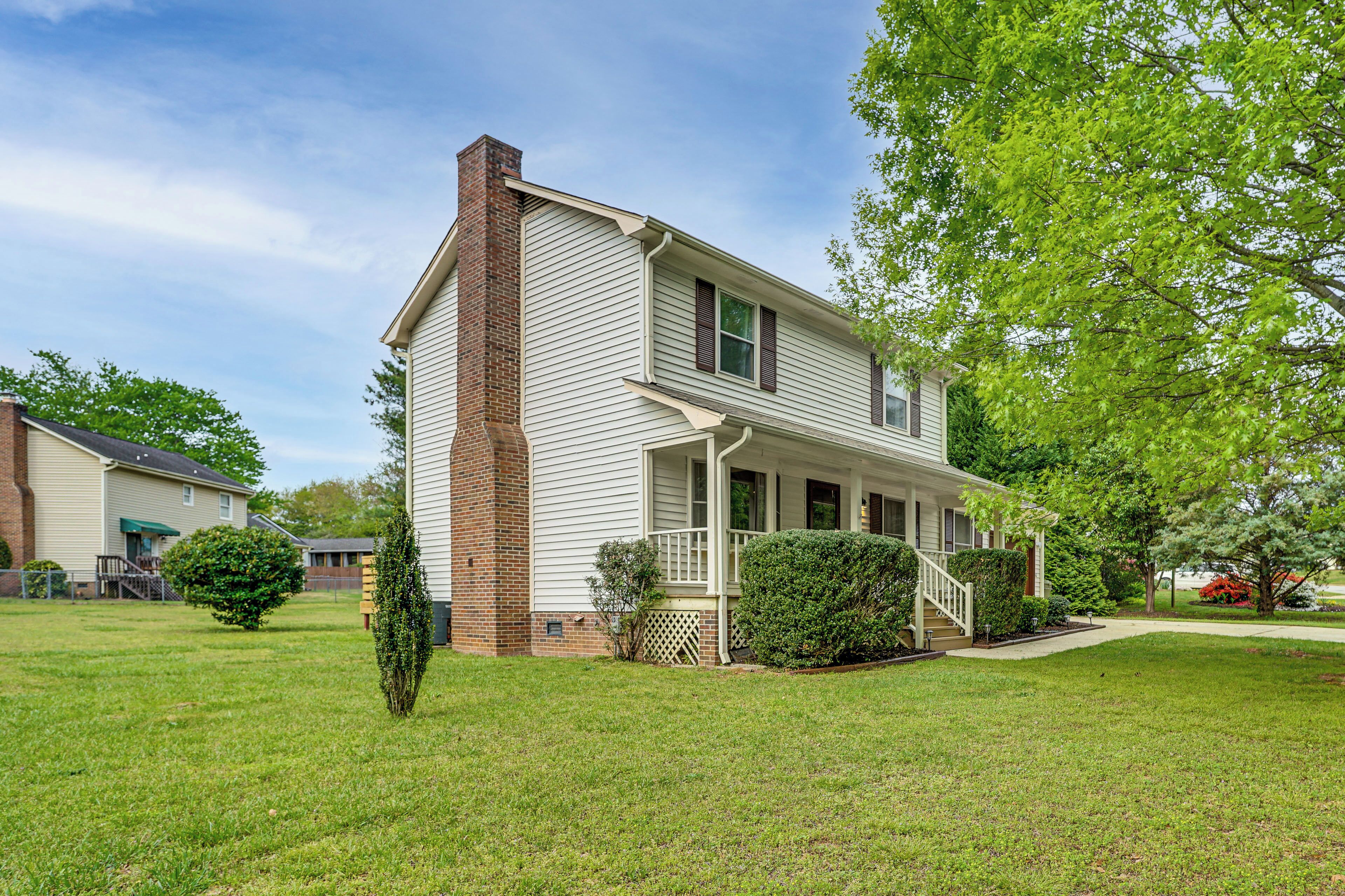 A two-story house with a brick chimney, a front porch, and a well-maintained lawn.