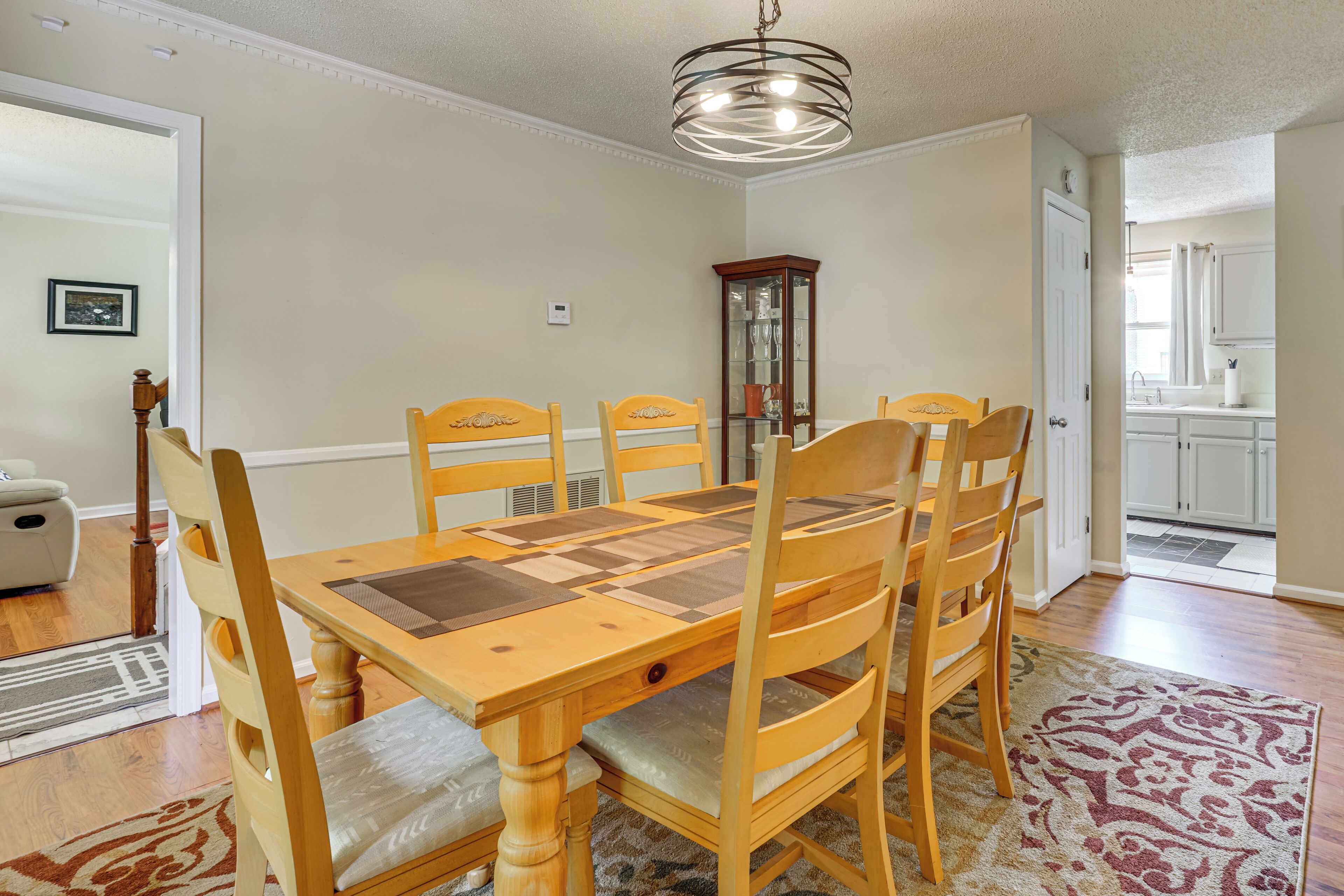 Een eetkamer met een houten tafel en stoelen, een kroonluchter en uitzicht op de keuken.