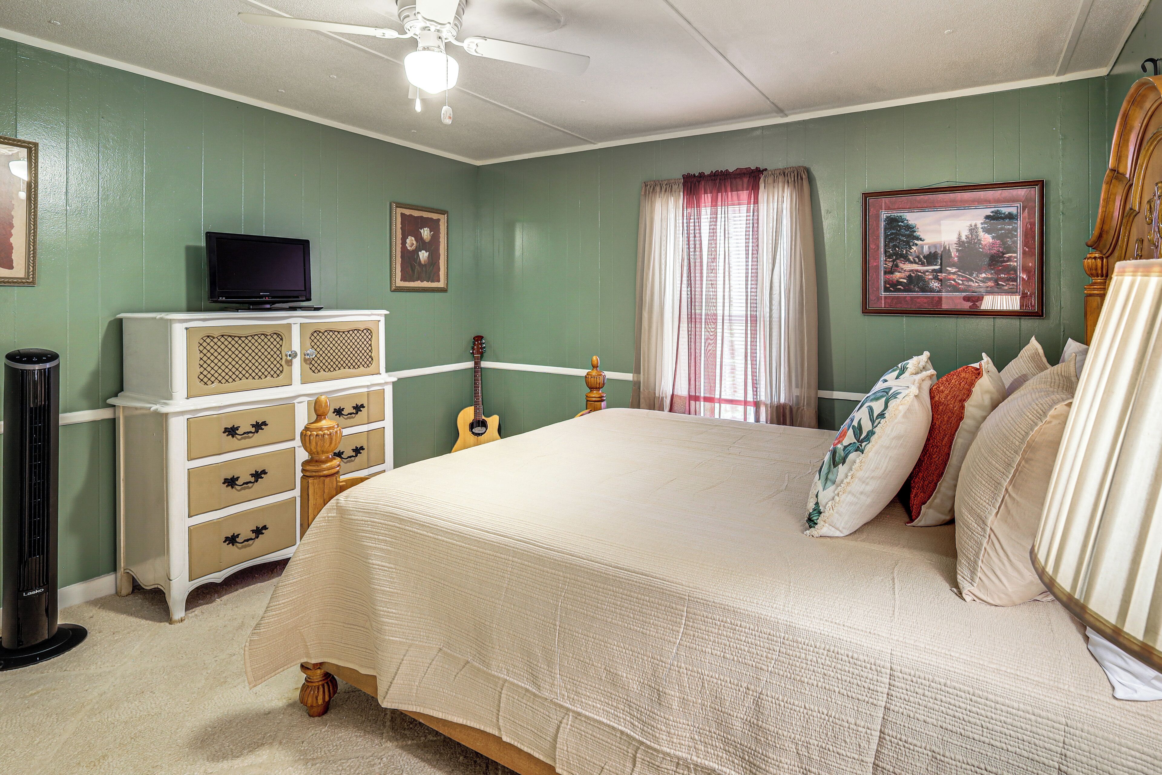 A bedroom with a bed, dresser, television, guitar, and framed pictures on the walls.