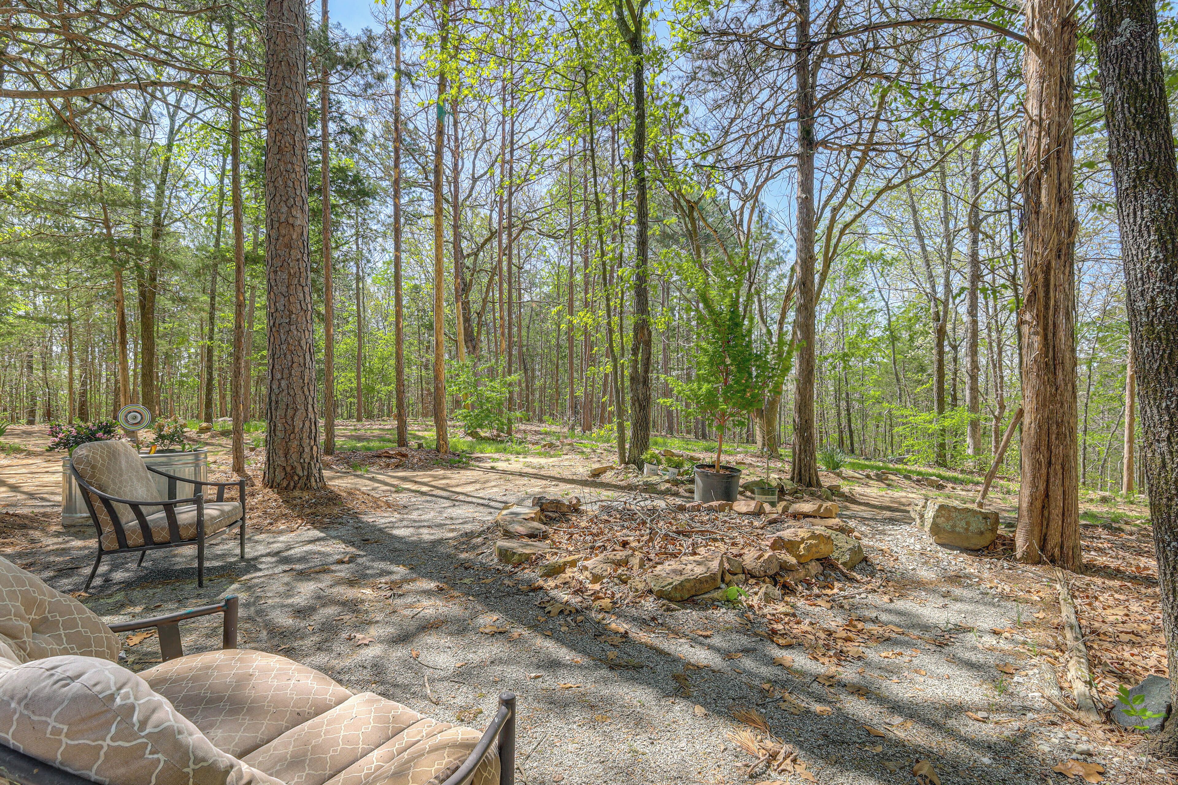 A forested area with a seating area, a table, and a fire pit.