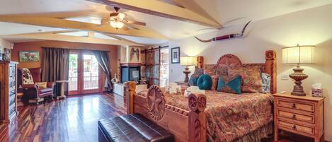 A spacious bedroom with a large bed, wooden headboard, a bench, a nightstand, and a ceiling fan.