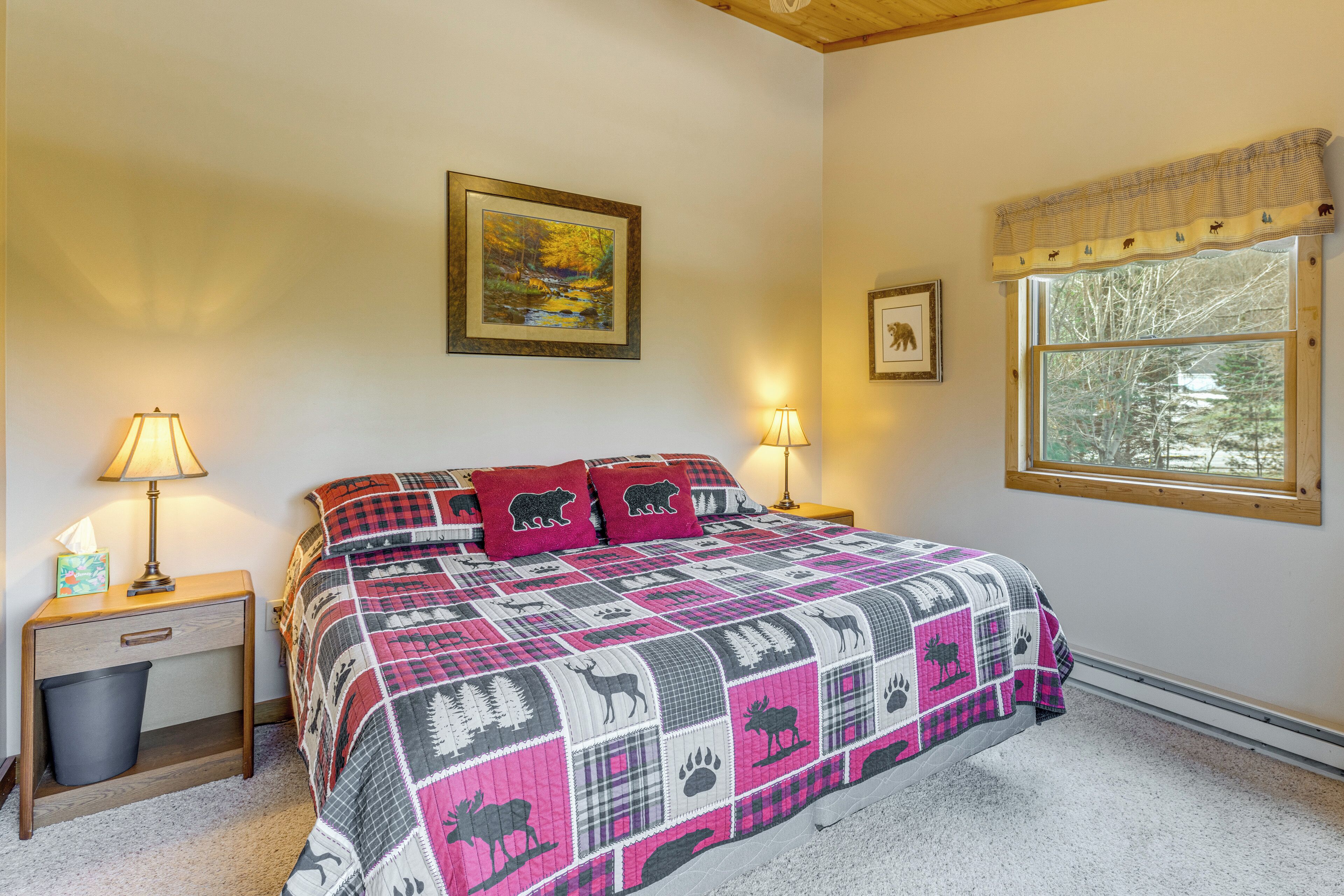 Een slaapkamer met een bed, twee nachtkastjes, een raam met uitzicht op bomen en een schilderij aan de muur.