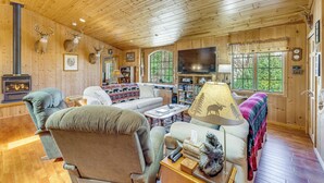 A log cabin interior with a fireplace, a sofa, a television, and a bookshelf. - On 4 Acres! Retreat w/ Lake Access in Maple City (Maple City)