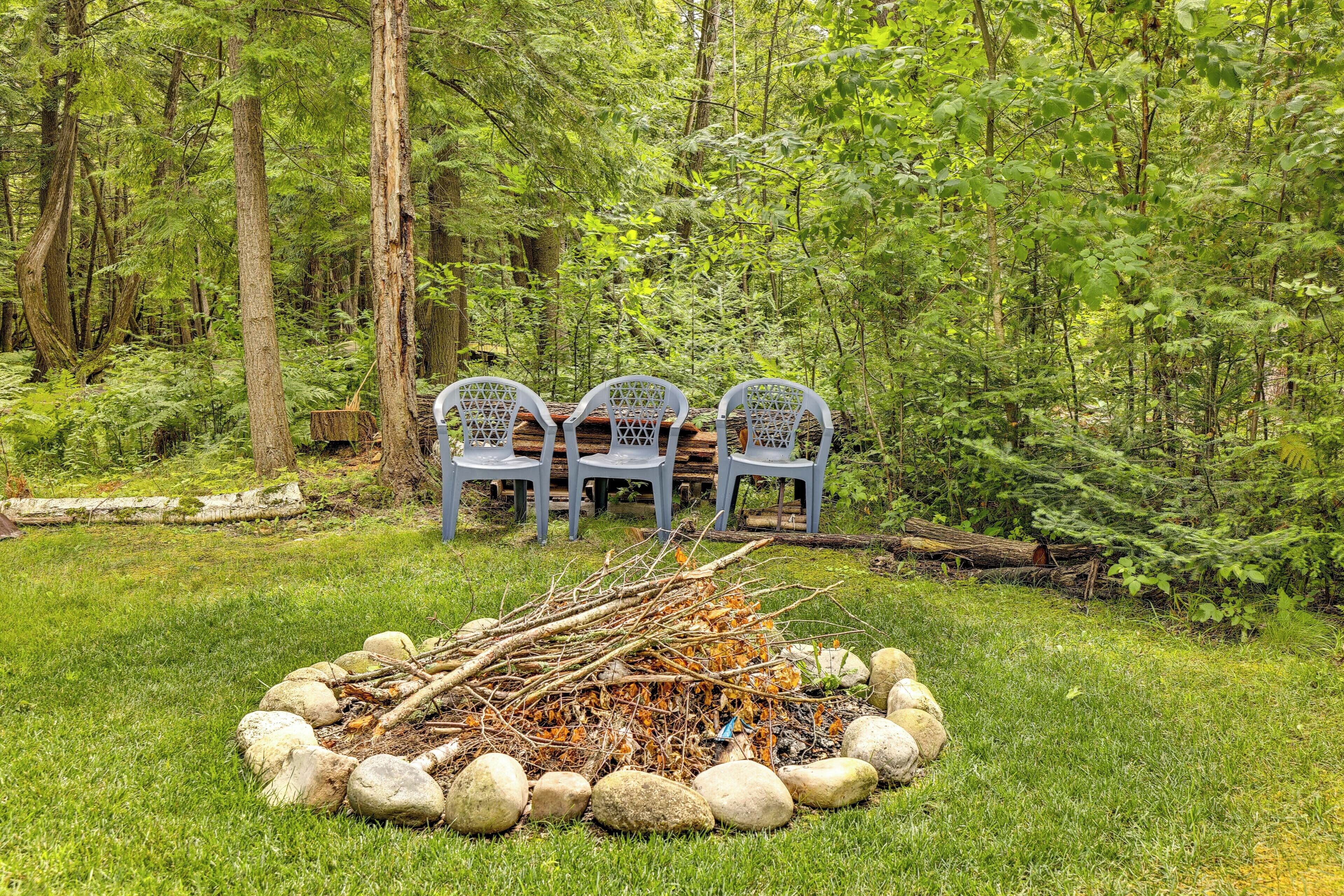 A natural outdoor setting with three chairs arranged around a fire pit surrounded by rocks.