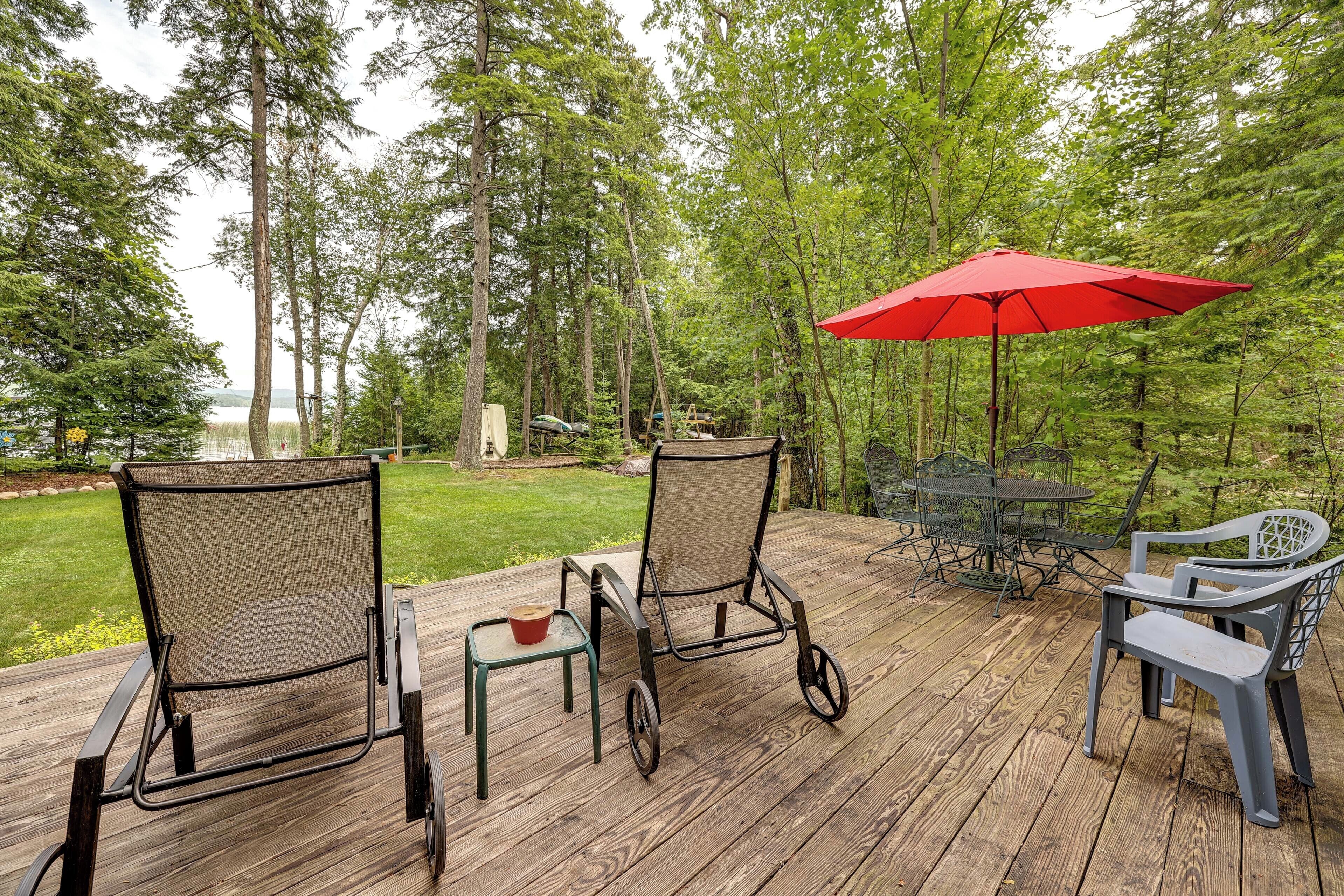 Une terrasse en bois avec des meubles d’extérieur, notamment des chaises et une table, et un parasol rouge pour faire de l’ombre.