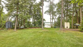 A grassy yard with a small shed, a hammock, and a boat docked by the water.