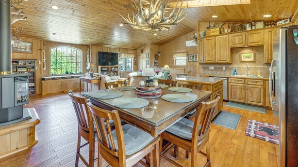 A spacious wooden interior with a large dining table, chairs, a fireplace, and a kitchen area. - On 4 Acres! Retreat w/ Lake Access in Maple City (Maple City)