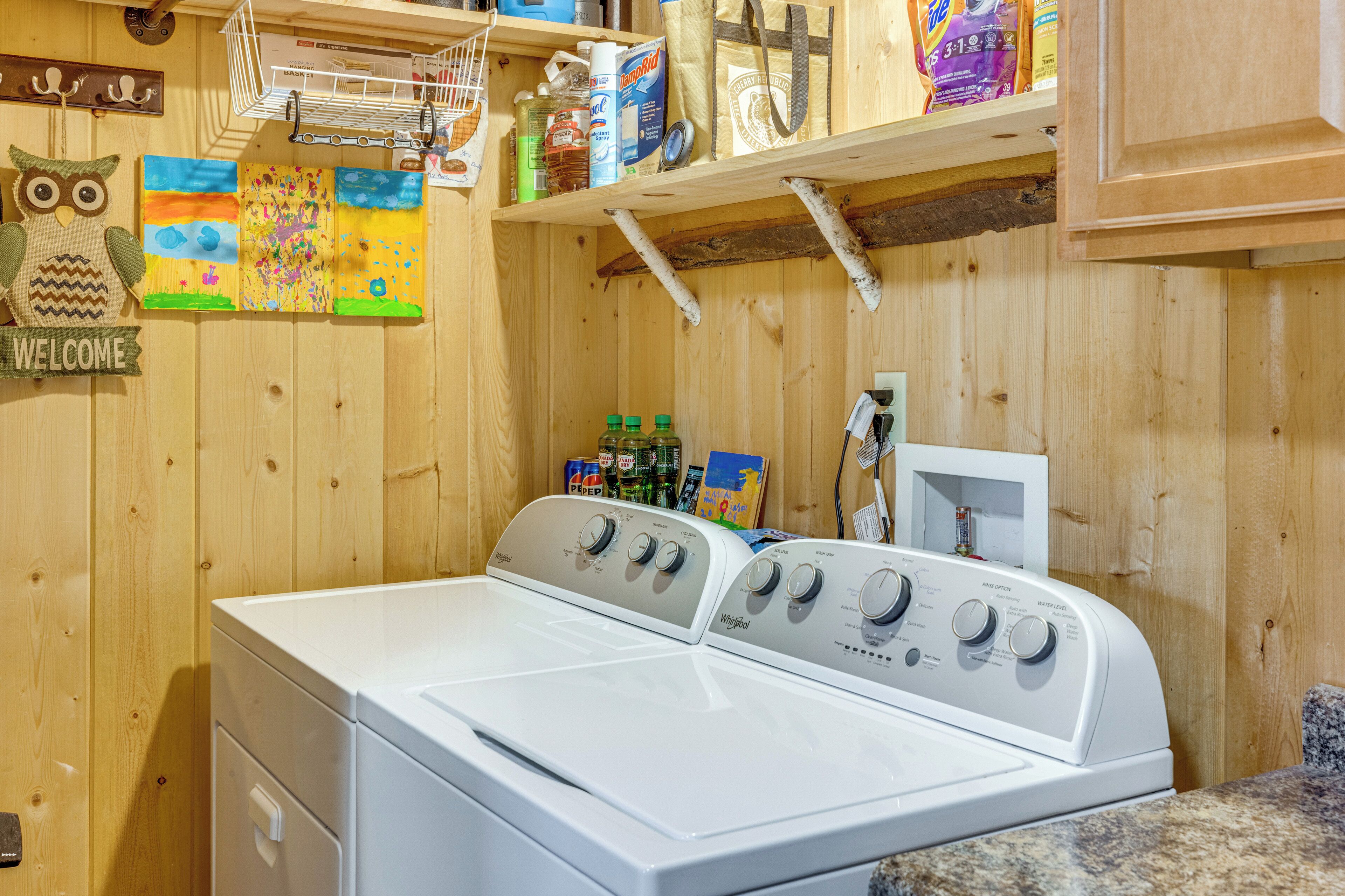 A laundry room with a front-loading washer and dryer, wooden walls, and various cleaning supplies on shelves.
