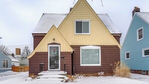 Une maison à deux étages aux couleurs marron et beige, avec une porte d’entrée et un petit porche.