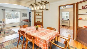 Un coin repas avec une table dressée pour quatre personnes, un lustre et une vue sur la cuisine par une porte ouverte.