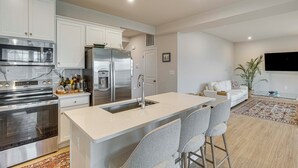 Een moderne keuken met roestvrijstalen apparatuur, een centraal eiland met barkrukken, een zithoek met een bank en een flatscreen televisie aan de muur.