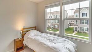 Een slaapkamer met een enkel bed, een nachtkastje en een raam met jaloezieën.