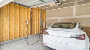 Een witte auto geparkeerd in een garage met houten wanden en zichtbare elektriciteitskabels.