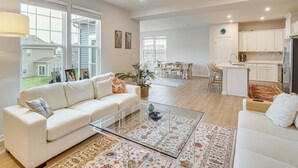 Een ruime woonkamer met een witte bank, een glazen salontafel, en een eethoek met stoelen en een tafel.
