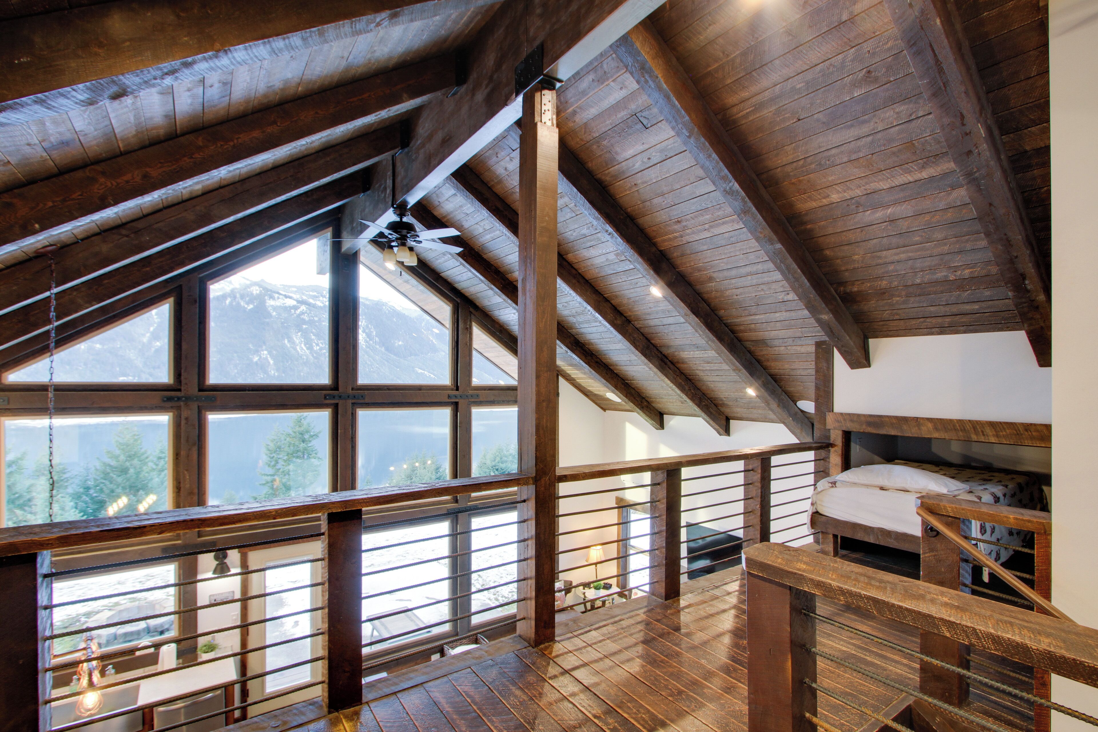 A spacious loft bedroom with a wooden ceiling and large windows overlooking a mountainous landscape.