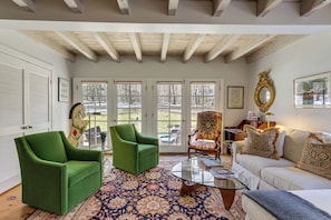 A room with a green armchair, a white sofa, a patterned rug, and a glass coffee table.