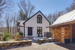 A house with a stone wall, a wooden bench, and a stack of firewood.