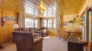 Interior acogedor de una cabaña con paredes de madera, chimenea, sofá, mesa de comedor y televisor.