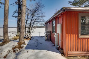 Una cabaña roja con una ventana, una puerta y una pequeña estructura adosada con una parrilla.