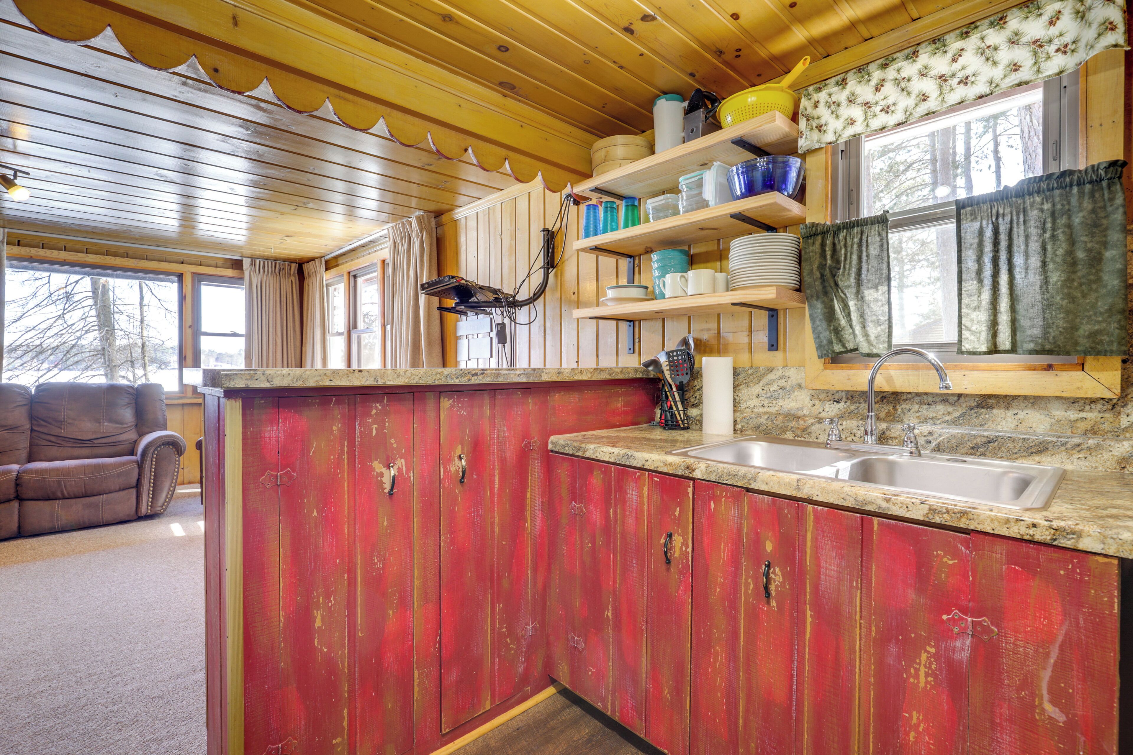 A kitchen with wooden cabinets, a granite countertop, a sink, and a window with curtains.