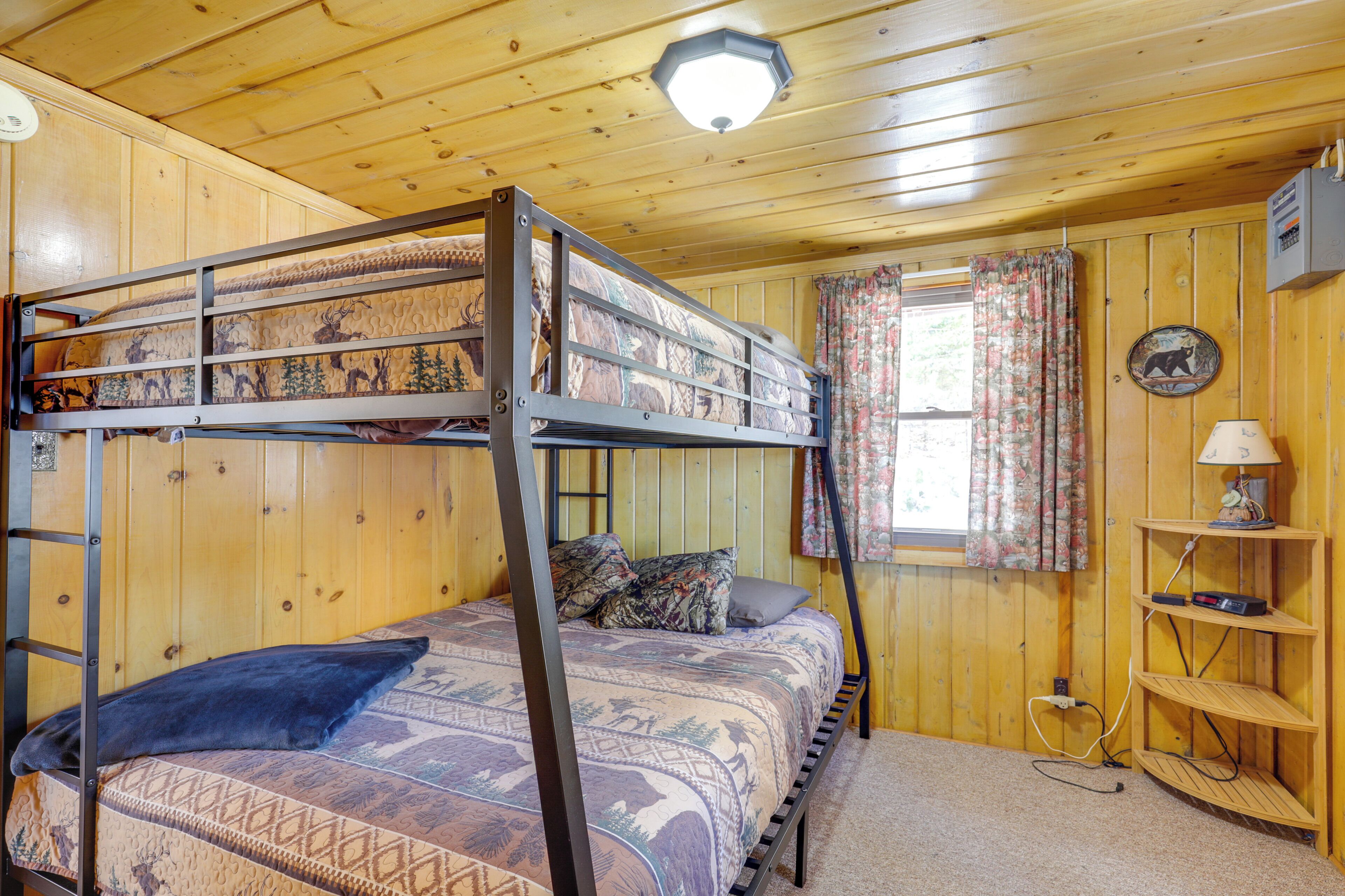 A bunk bed with patterned bedding, a lamp on a shelf, and a window with curtains.