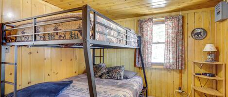 A bunk bed with patterned bedding, a lamp on a shelf, and a window with curtains.
