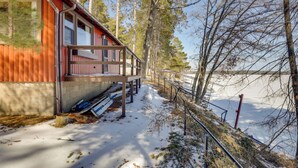En stuga med en träveranda, ett snötäckt område och en skog i bakgrunden.