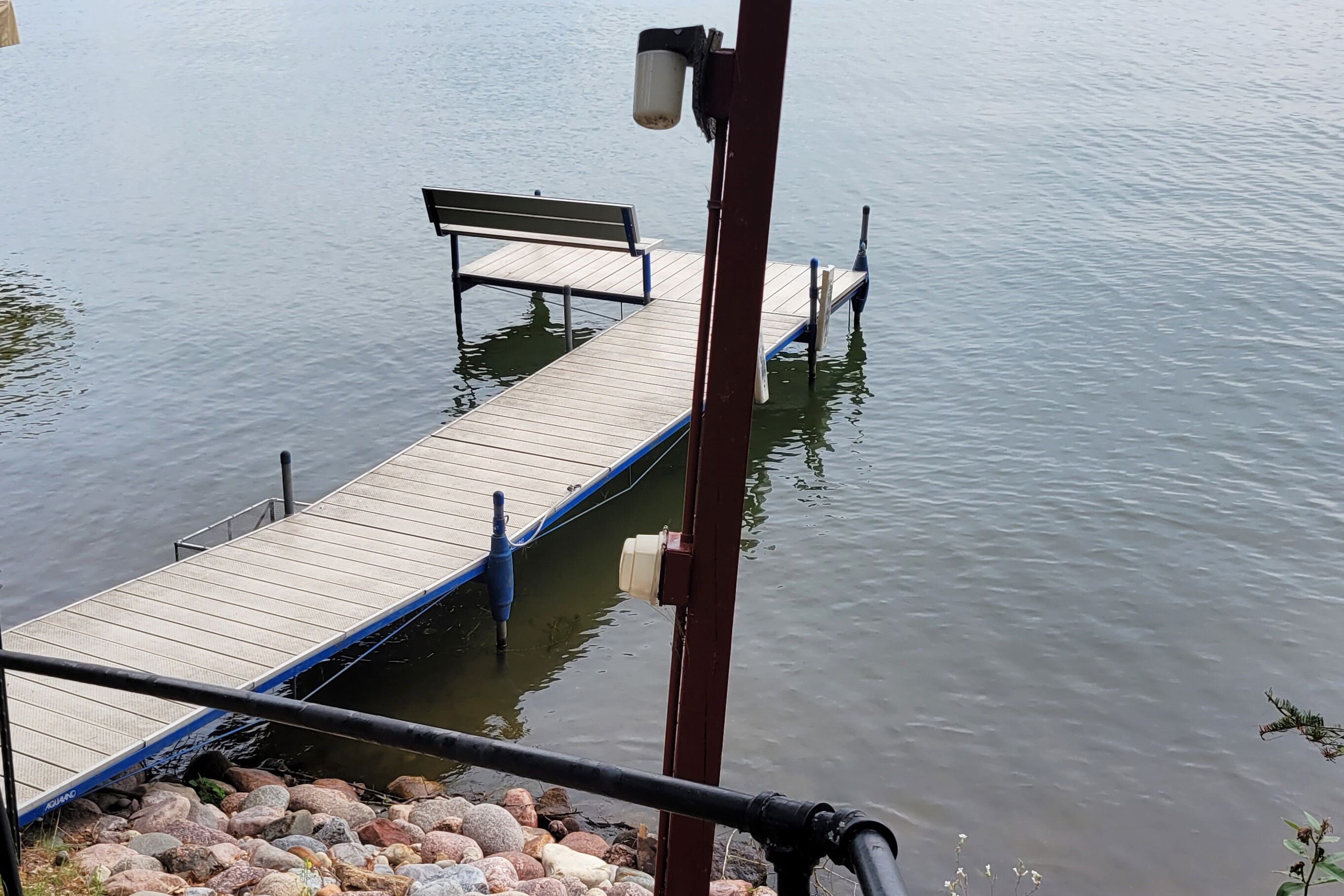 A wooden dock extending into calm water, a bench, and a railing.