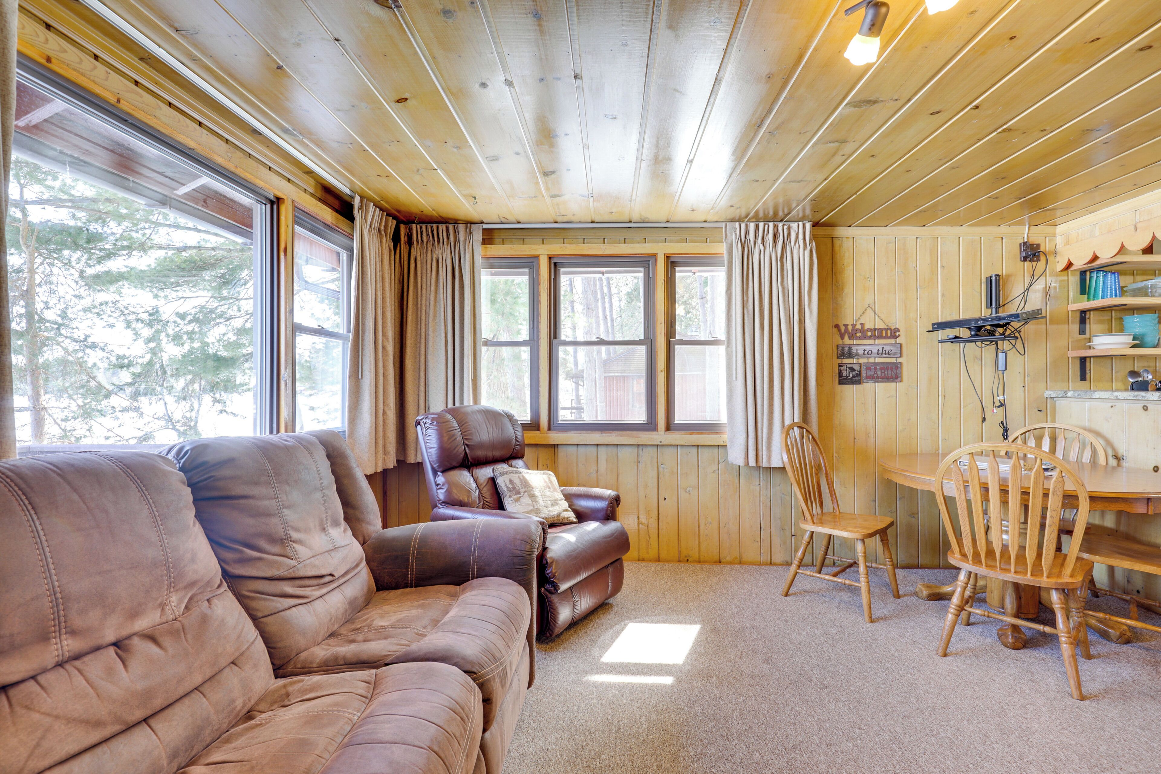 Un interior de madera con un sofá, un sillón reclinable, una mesa de comedor con sillas y una ventana con cortinas.