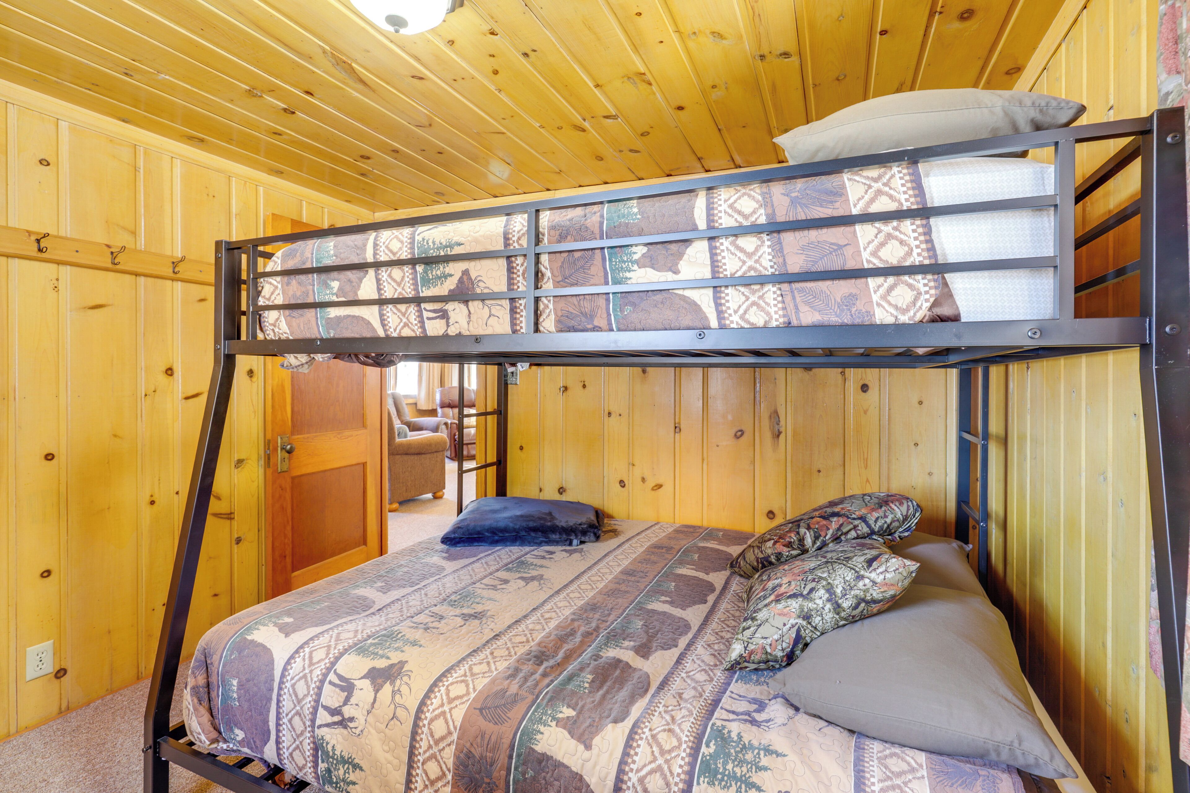 A bunk bed with patterned bedding, wooden walls, and a door leading to another room.