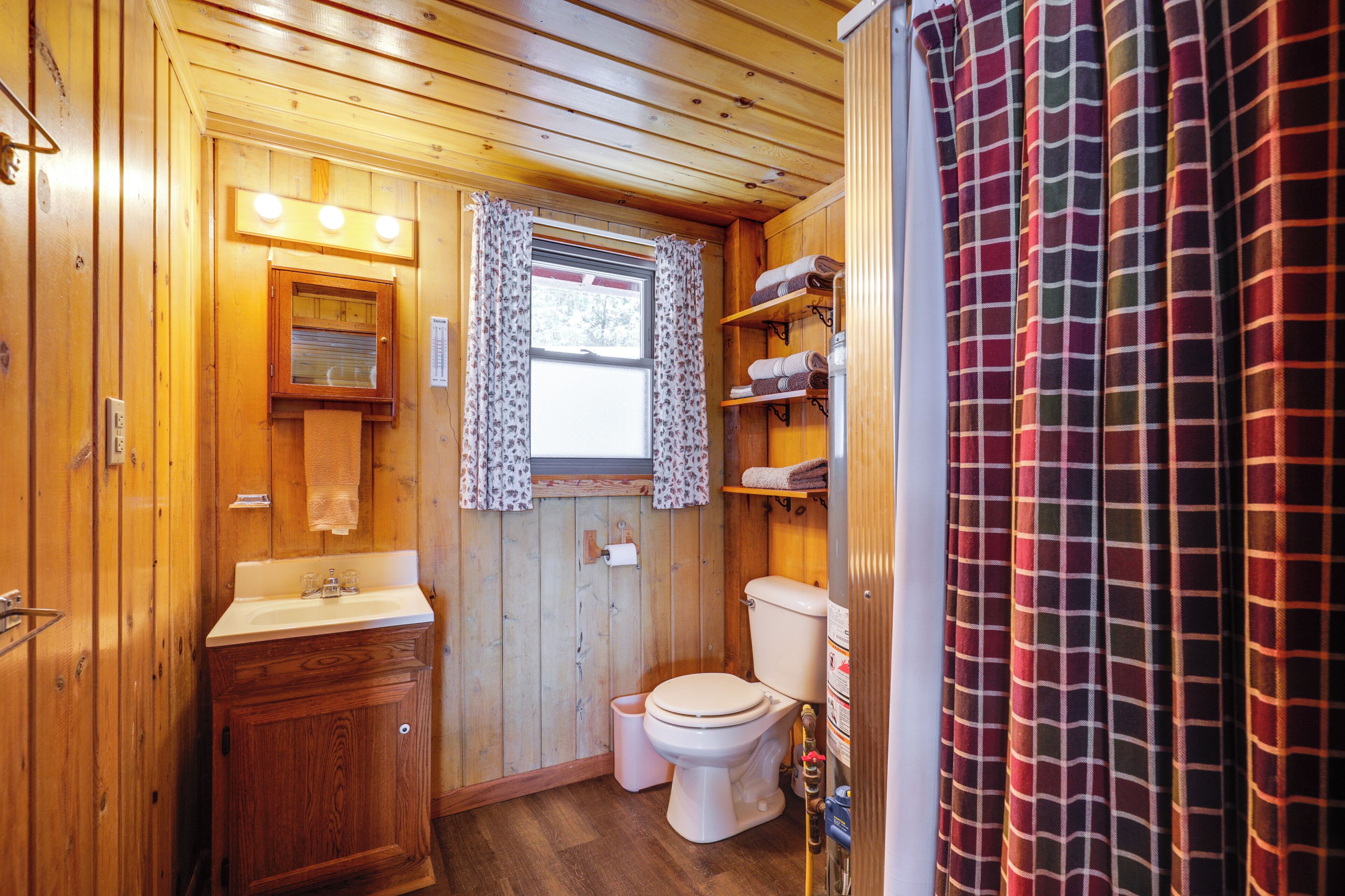 A compact wooden bathroom with a sink, toilet, and a window with curtains.