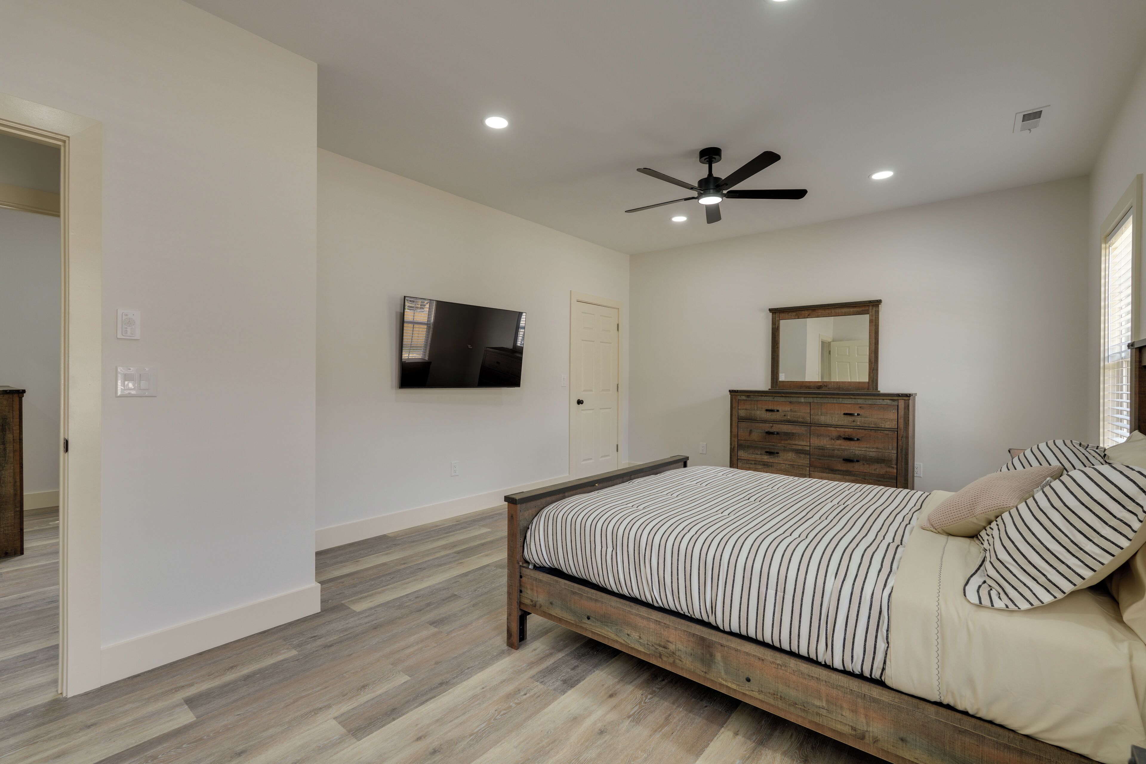 Une chambre à coucher avec un lit, un ventilateur de plafond, une télévision, une commode et un miroir.