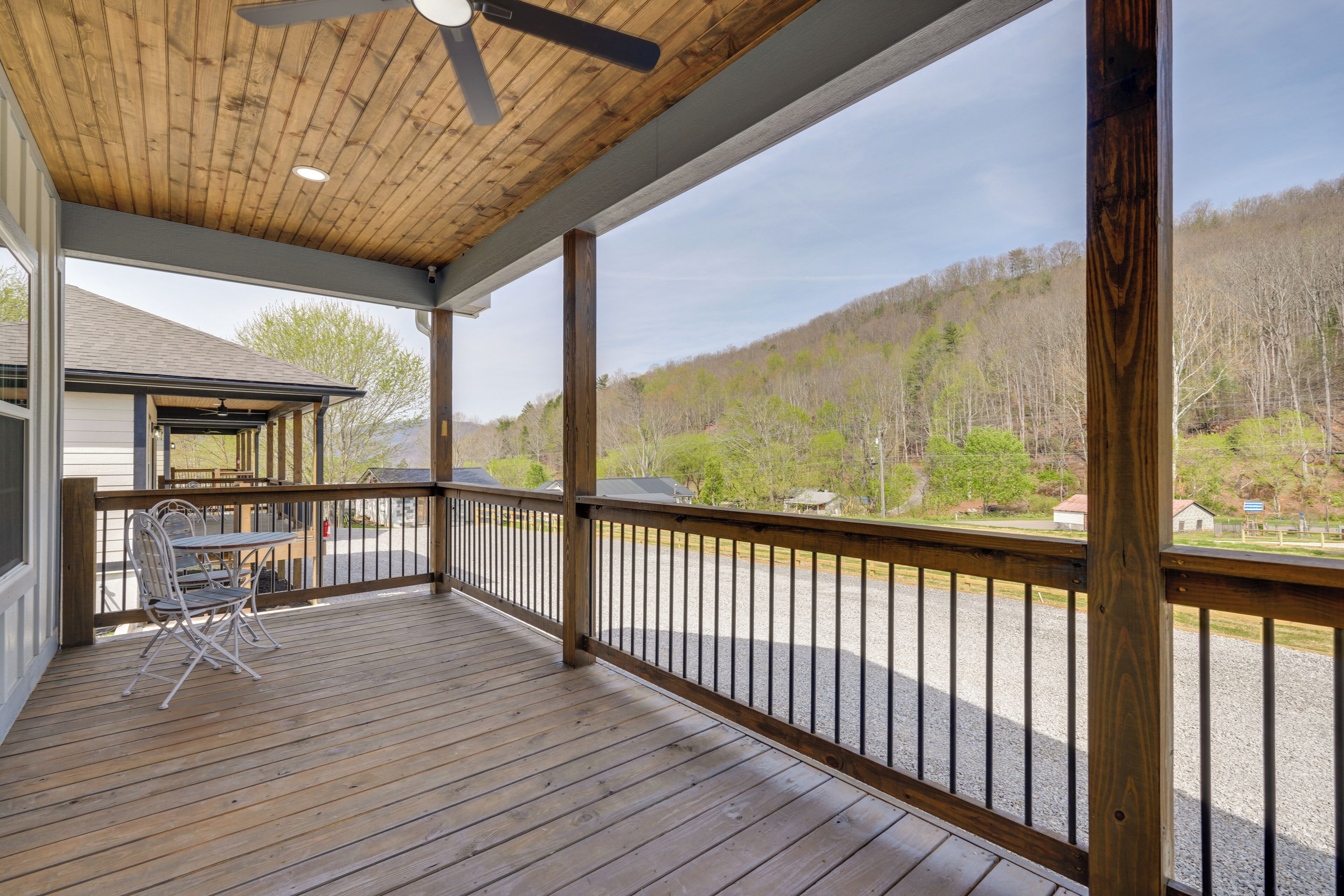 Un espace extérieur abrité, doté d’une terrasse en bois, d’une table avec des chaises et offrant une vue sur une colline boisée.