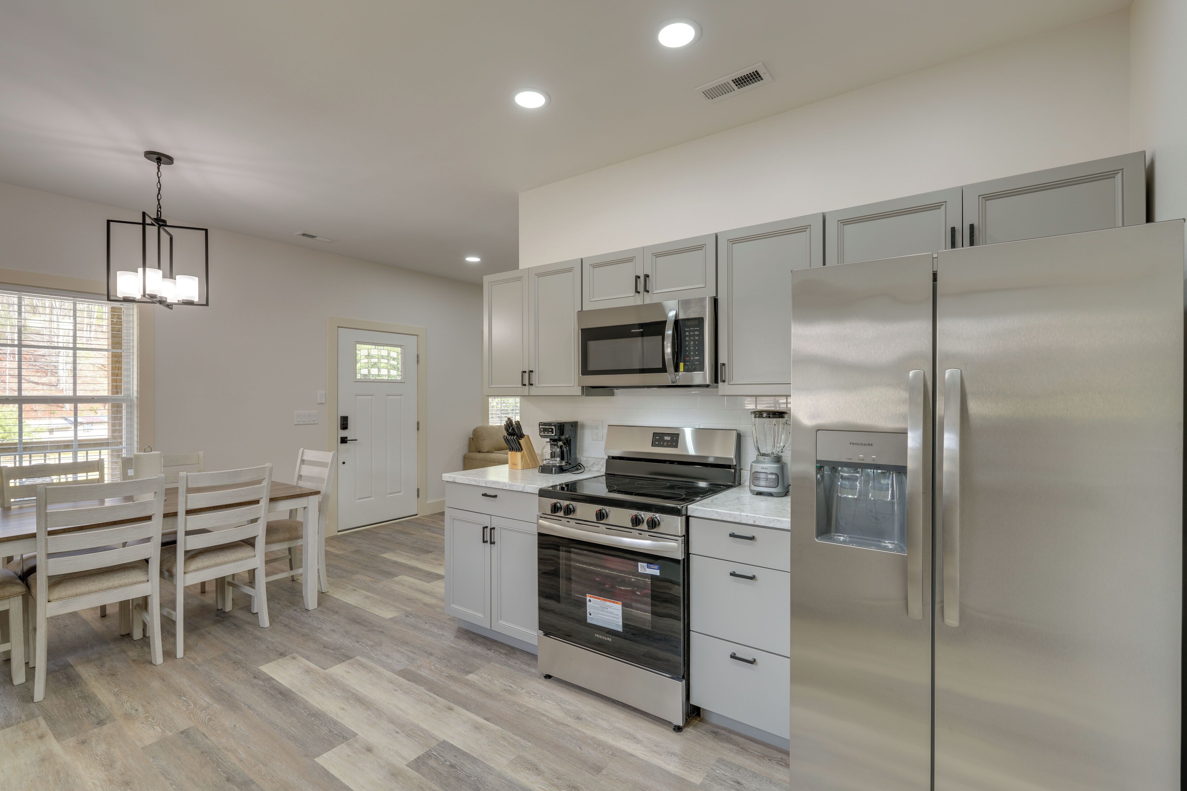 A modern kitchen with stainless steel appliances, a dining table with chairs, and a window with blinds.