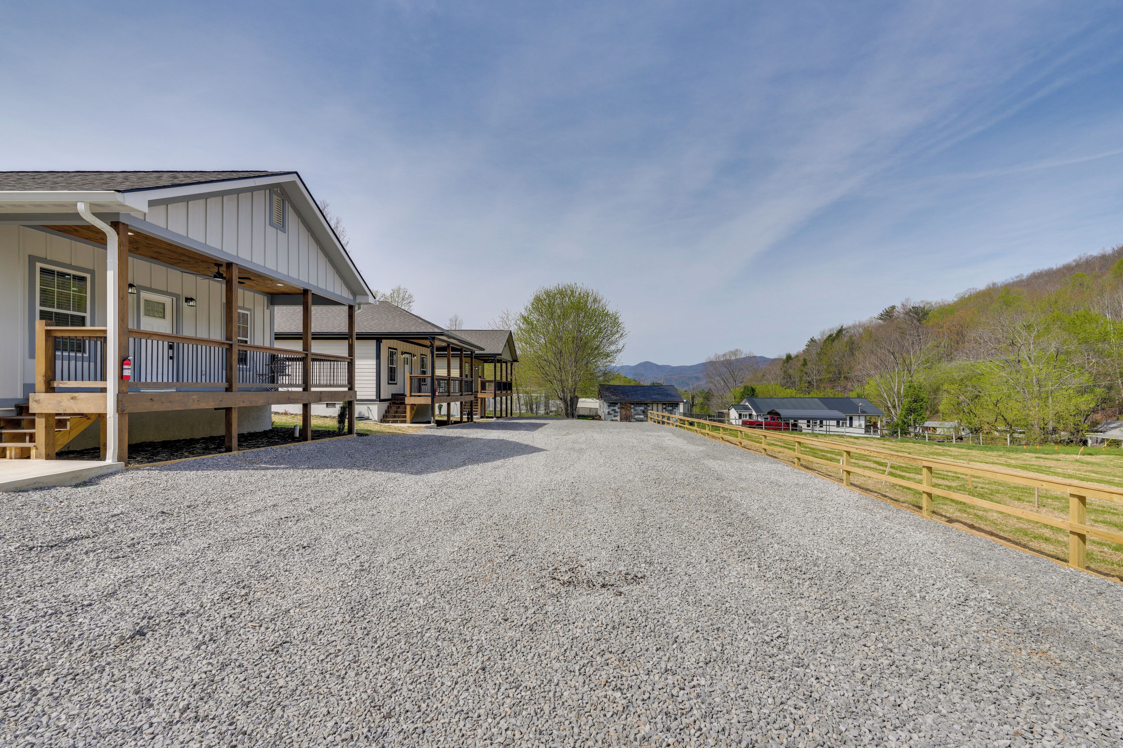 A building with a covered outdoor area, a gravel driveway, and a fenced area with a red building in the background.