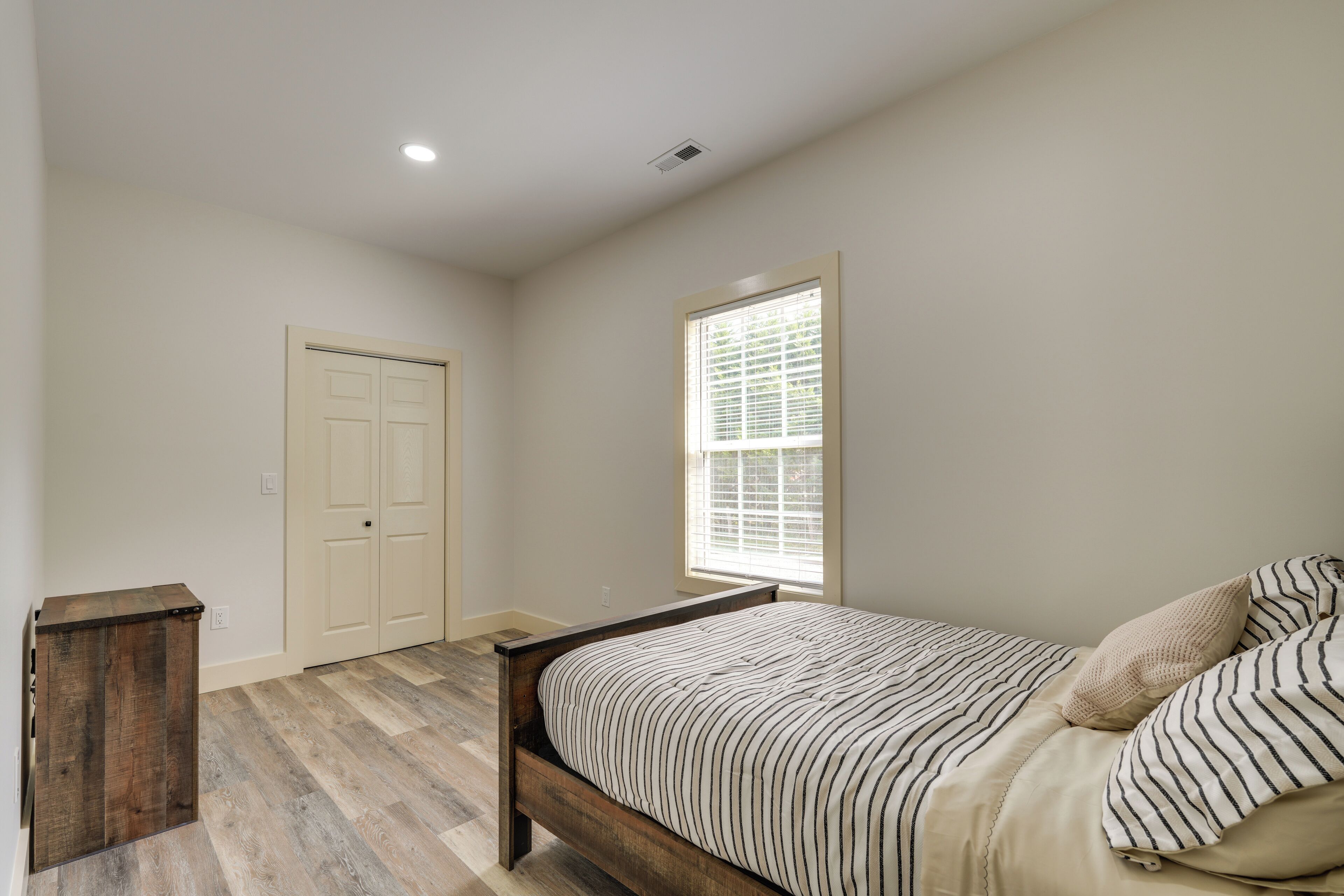 Une chambre à coucher avec un lit, une fenêtre, une porte et une petite armoire en bois.