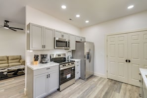 A modern kitchen with stainless steel appliances, a built-in oven, and a refrigerator. There is a dining table with chairs and a sofa in the adjacent living area. - 4 Mi to Nolichucky River Adventures! Mtn-view Home (Erwin)