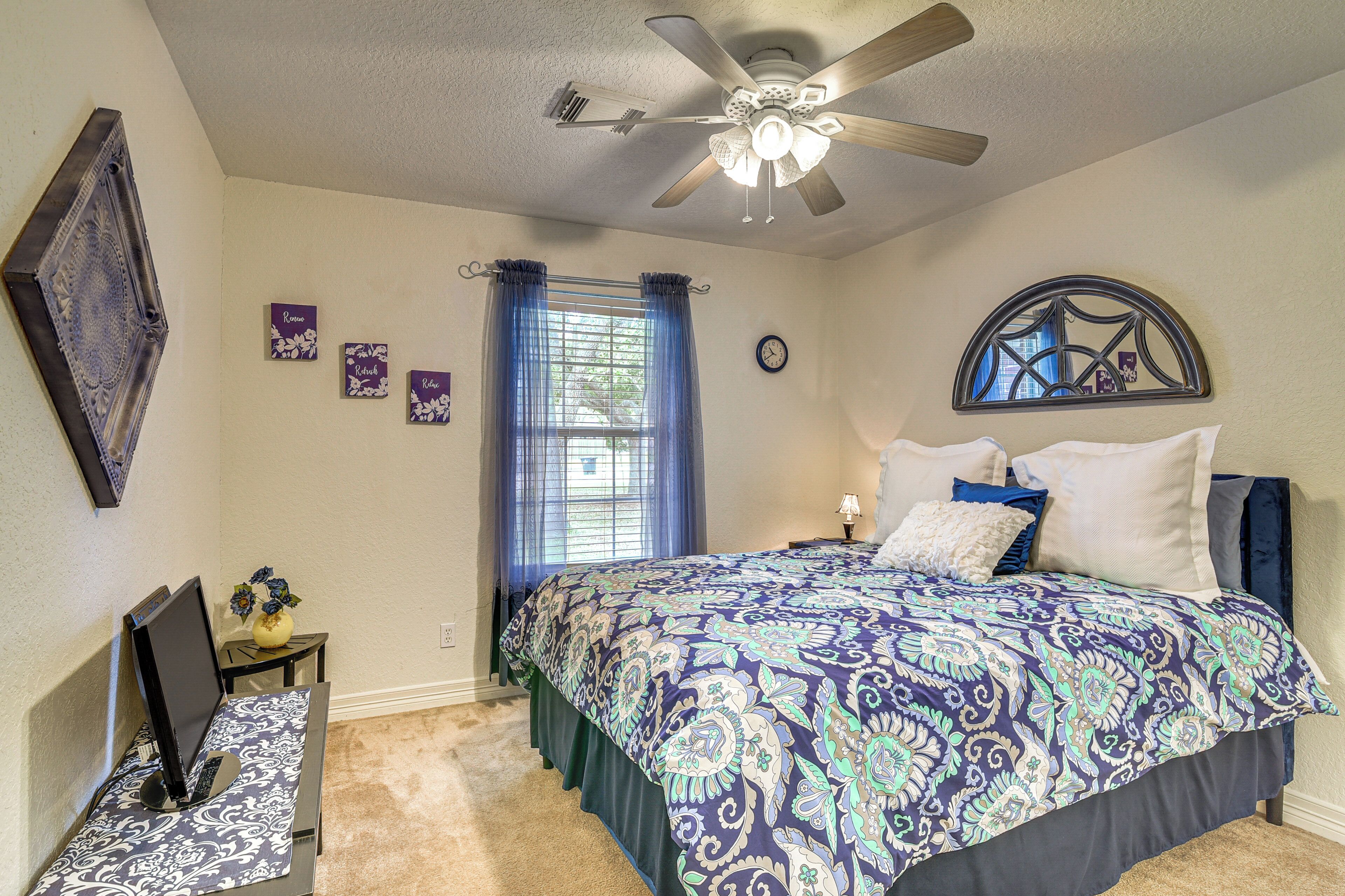 Une chambre à coucher comprenant un lit, un ventilateur de plafond, un bureau avec un ordinateur, une fenêtre avec des rideaux et des éléments de décoration murale.
