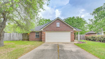 A single-story brick house with a garage, a driveway, and a tree in the yard.