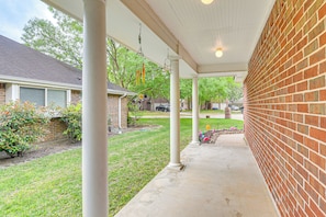 A covered patio with a brick wall, white columns, and a lawn area.