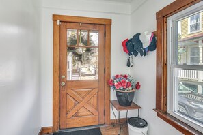 Eine Holztür mit Glasfenster, ein kleiner Tisch mit Blumentopf und ein Fenster mit Blick auf geparkte Autos.