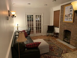 Un salon comprenant un canapé, une cheminée, un tapis à motifs et une porte donnant sur une autre pièce.