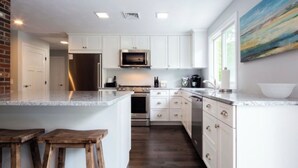 A modern kitchen with white cabinetry, a central island, and a large window. - Located directly on Pond, Swimming, Kayaking, Fishing, Beach Pass, A/C, Clean! (Barnstable)